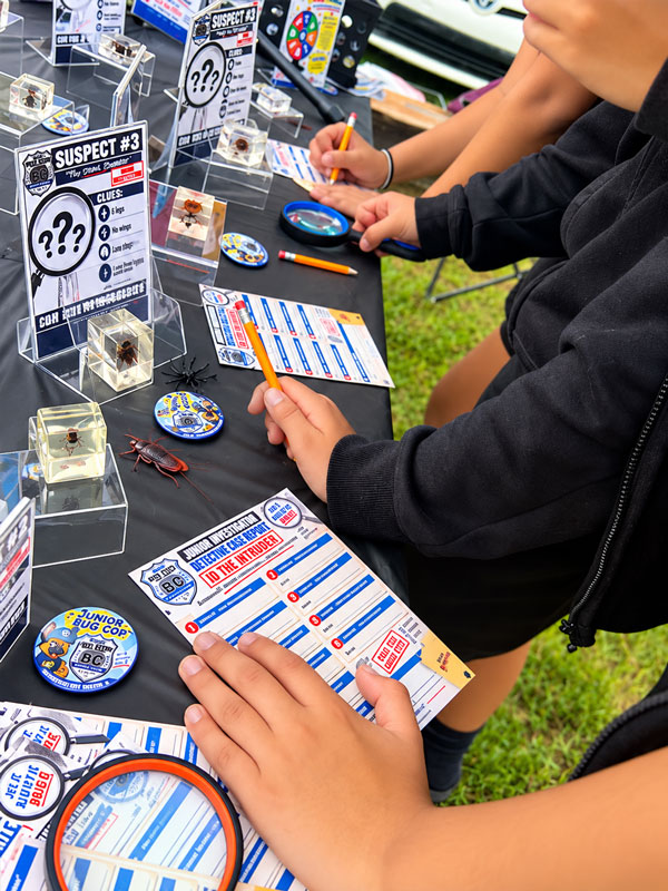 Children completing Junior Bug Cop identification worksheets while examining preserved insect specimens and clue cards at the Florahome Fall Heritage Festival.