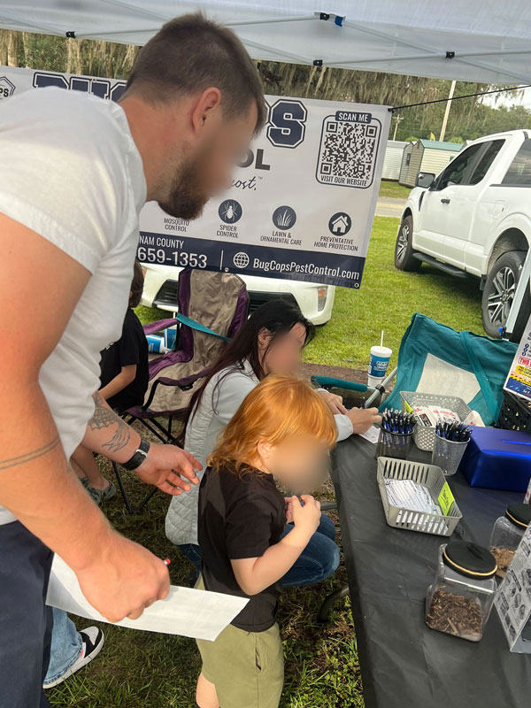 Adult and child examining pest identification displays and specimens at the Bug Cops Evidence Table during the Florahome Fall Heritage Festival.