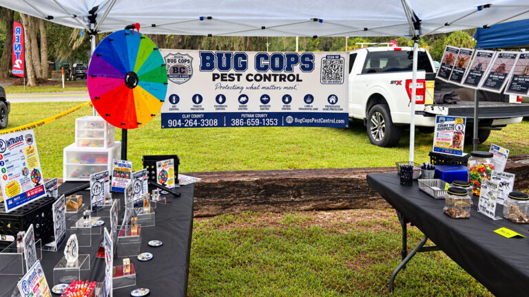 Bug Cops Pest Control booth at the Florahome Fall Heritage Festival in North Florida, featuring pest identification displays, a colorful prize wheel, and the company banner.